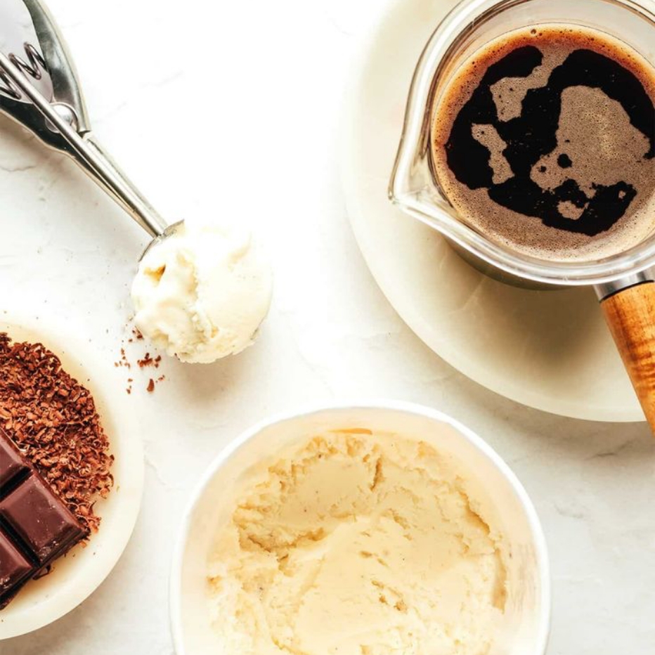 .מרכיבים להכנת אפוגטו: כדור גלידת וניל בכף מתכת, קוביות שוקולד מגורדות, קערית גלידה פתוחה וקנקן קפה שחור