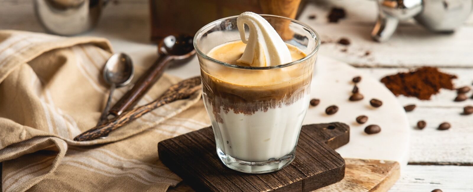 .גלידת אפוגטו בטעם וניל עם קפהאפוגטו בכוס זכוכית – גלידת וניל עם אספרסו מעל, מונחת על תחתית עץ, מוקפת פולי קפה טחונים וכפית מתכת