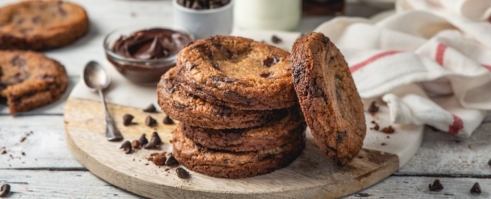 .עוגיות שוקולד צ׳יפס על קרש עץ, עם חלב ושוקולד ברקע